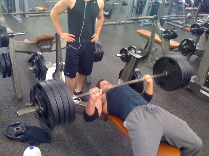 Chad bench pressing a heavily loaded barbell while a spotter stands behind him